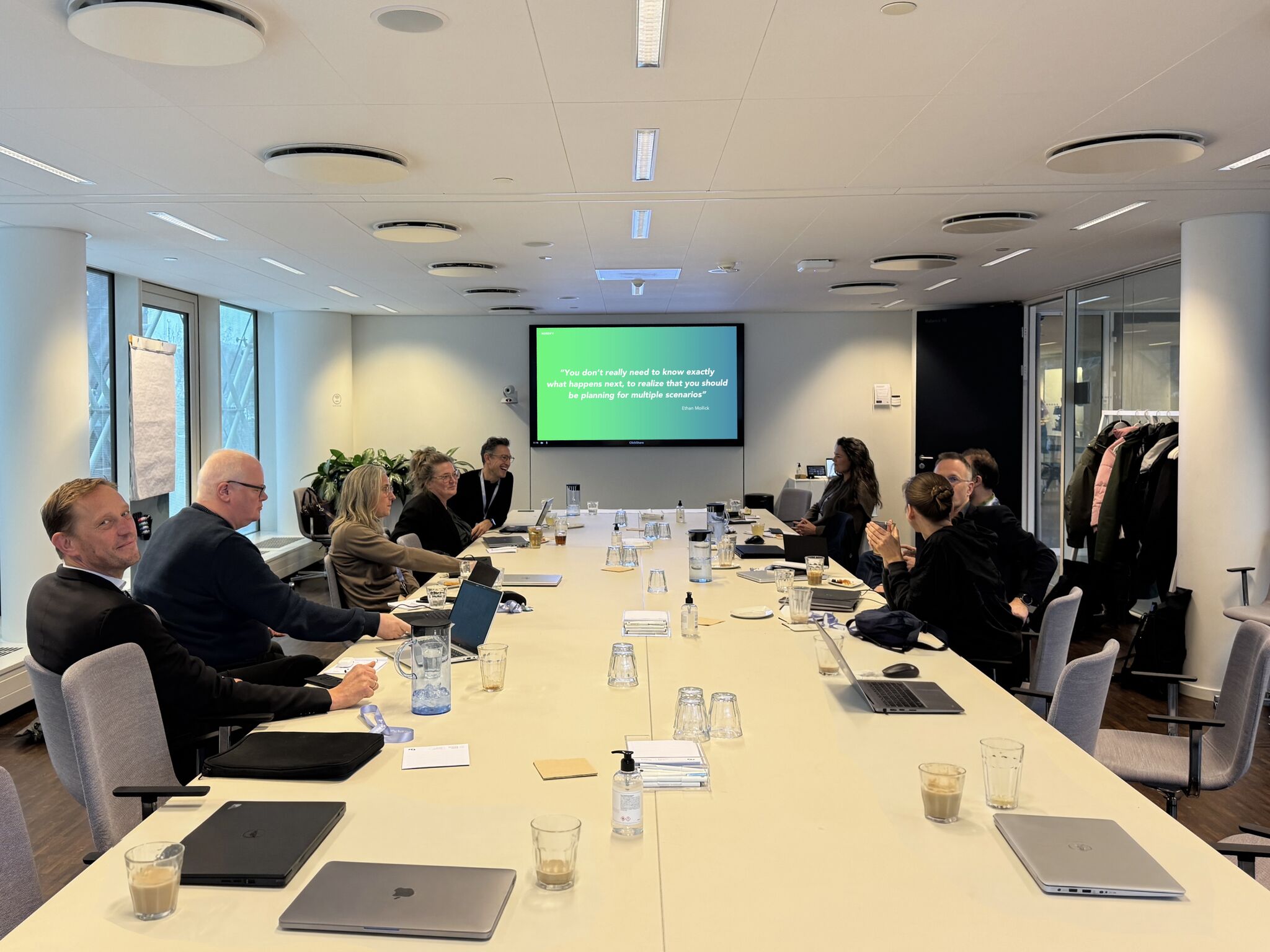 Deltagere i en Accelerator-session diskuterer rundt om et langt mødebord med en præsentation på skærmen.
